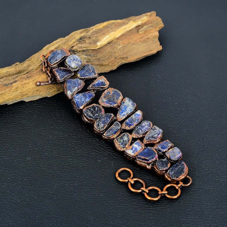 K&ouml;nnte beinhalten: Ein Kupferarmband mit einer Reihe von dunkelblauen und violetten Edelsteinen. Die Steine sind unregelm&auml;&szlig;ig geformt und haben eine raue, nat&uuml;rliche Textur.