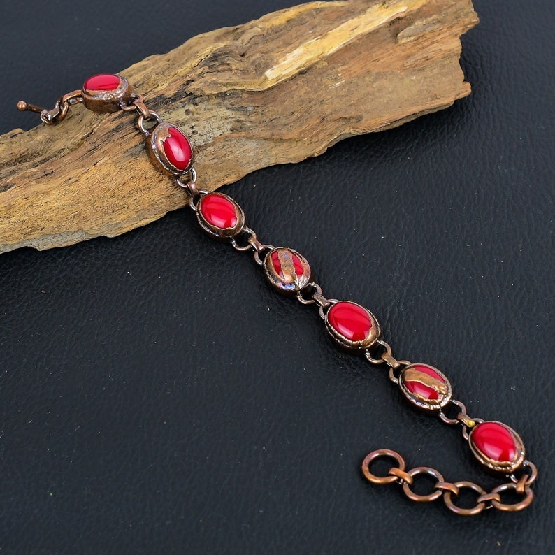 K&ouml;nnte beinhalten: Ein Kupferarmband mit roten ovalen Steinen. Das Armband hat einen Karabinerverschluss.