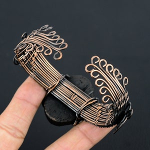 May include: A copper wire bracelet with a black stone center and intricate wire designs on each side. The bracelet is woven with copper wire and has a delicate, intricate design.
