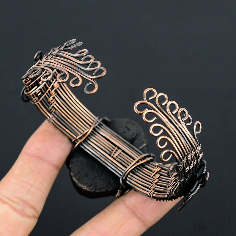 May include: A copper wire bracelet with a black stone center and intricate wire designs on each side. The bracelet is woven with copper wire and has a delicate, intricate design.