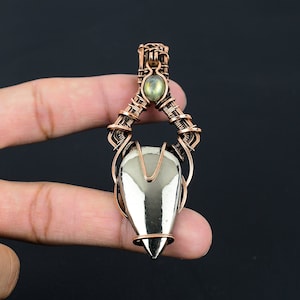 May include: A copper wire wrapped pendant featuring a silver-toned gemstone and a smaller green gemstone. The pendant is designed in a geometric shape with a pointed bottom.