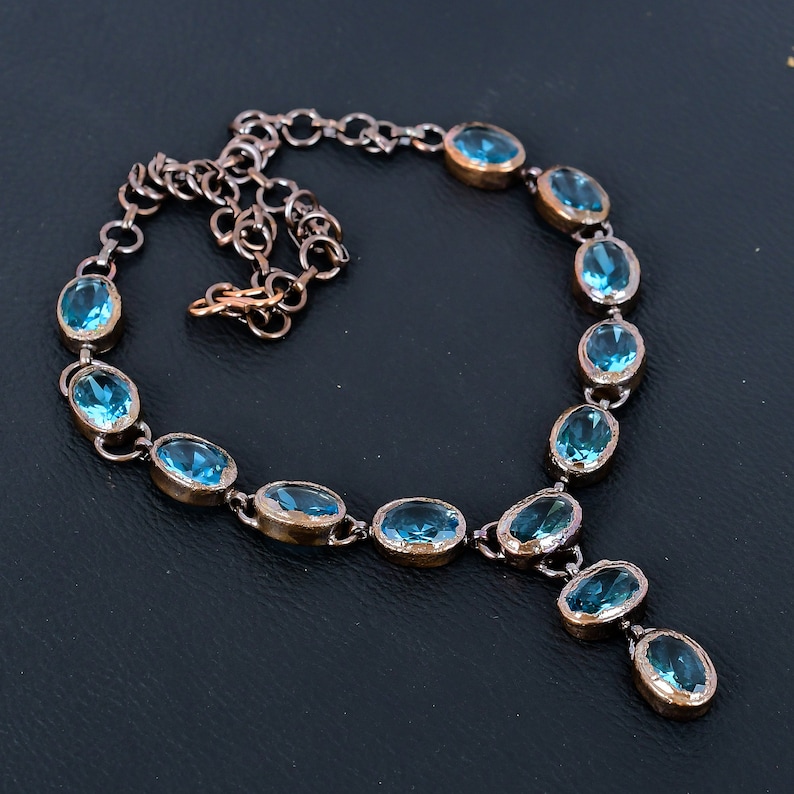 May include: A copper chain necklace with oval shaped blue gemstones. The necklace has a pendant with three blue gemstones.