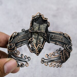 May include: A black and silver wire wrapped bracelet with a black and white fossilized stone centerpiece.
