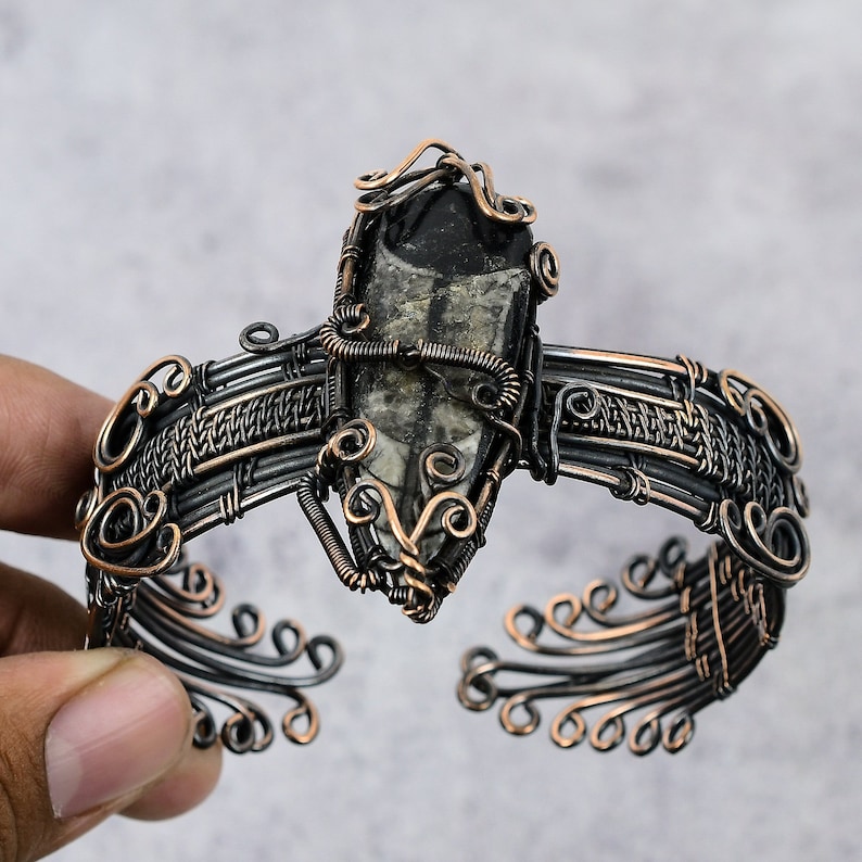 May include: A black and silver wire wrapped bracelet with a black and white fossilized stone centerpiece.
