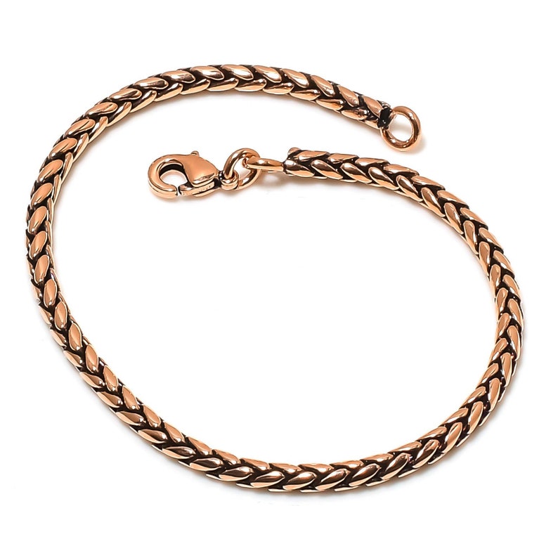 May include: A rose gold braided chain bracelet with a lobster clasp closure.