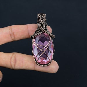 May include: A pink gemstone pendant wrapped in copper wire. The pendant is oval shaped and has a faceted design. The wire is wrapped around the stone in a decorative pattern.