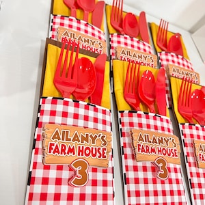 May include: Red and white checkered paper place setting with a wooden sign that says "Ailany's Farm House 3". The place setting includes a red fork, spoon, and knife.