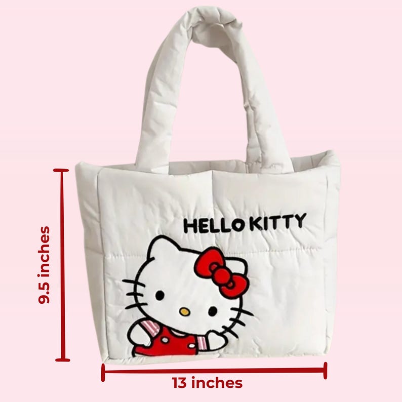 Puede incluir: Bolso tote acolchado blanco con un gr&aacute;fico de Hello Kitty. El bolso tiene un lazo rojo, un vestido rojo y las palabras "HELLO KITTY" en negro. El bolso mide 24 cm de alto y 33 cm de ancho.