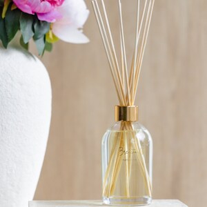 May include: A clear glass bottle with a gold lid and wooden sticks inside. The bottle is filled with a light yellow liquid and has a label that reads "Briarwood" with the text "natural essences" underneath.