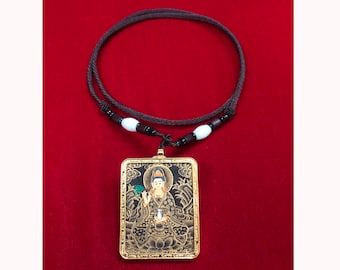May include: A gold pendant necklace featuring a rectangular image of a deity in a seated pose. The pendant is framed in gold and hangs from a brown cord with white beads.