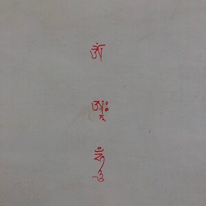 May include: Three lines of red Tibetan script on a white background. The script reads "Om Ah Hum".