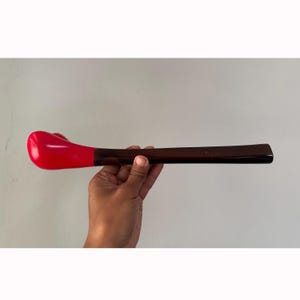 Puede incluir: Una cuchara de mango largo de madera marrón con un cuenco rojo en forma de corazón.