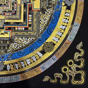 May include: A detailed mandala with intricate patterns and gold accents. The mandala is surrounded by a blue and gold border with Tibetan script. The mandala is on a black background.
