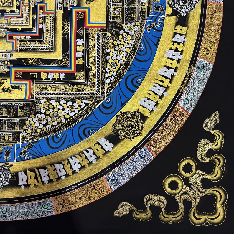May include: A detailed mandala with intricate patterns and gold accents. The mandala is surrounded by a blue and gold border with Tibetan script. The mandala is on a black background.