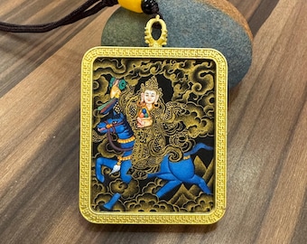 May include: A gold-coloured pendant with a rectangular frame, featuring a detailed illustration of a deity riding a blue horse against a black background. The pendant is suspended by a black cord with a yellow bead.