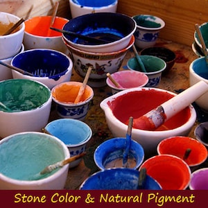 May include: A collection of small bowls filled with different colored pigments, used for creating natural stone colors. The bowls are arranged on a wooden surface, with some of the pigments still wet and others dried.