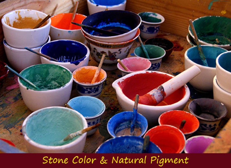 May include: A collection of small bowls filled with different colored pigments, used for creating natural stone colors. The bowls are arranged on a wooden surface, with some of the pigments still wet and others dried.