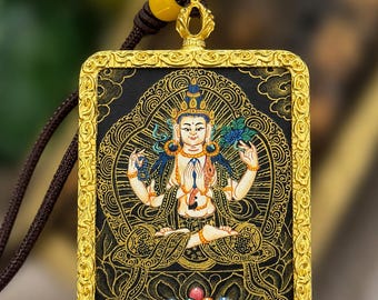 May include: A rectangular pendant featuring a central figure with multiple arms in a seated pose, rendered in gold and colors against a black background. The pendant is framed by an ornate gold border and hangs from a dark brown cord with a yellow bead.