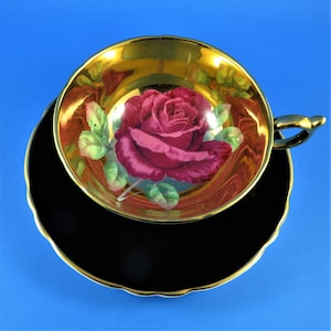 May include: A black and gold teacup and saucer set with a single red rose painted on the inside of the cup.