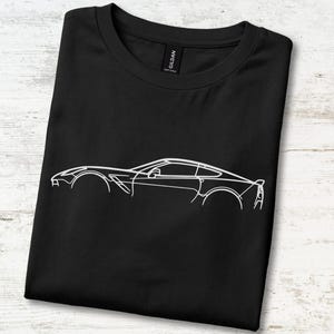 May include: A black short-sleeved t-shirt featuring a white line art graphic of a sports car silhouette on the front. The shirt has a crew neckline and a Gildan brand label visible at the inner collar, showcasing a clean and simple design.