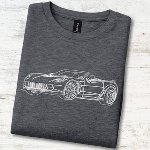 Op de afbeelding: Een donkergrijs gemêleerd t-shirt met een witte lijntekening van een cabriolet sportwagen op de voorzijde. Het shirt heeft een ronde hals en een zwart Gildan-merklabel dat zichtbaar is aan de binnenkant van de kraag van het kledingstuk.