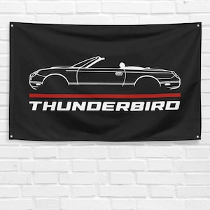 Może przedstawiać: Czarno-biała sylwetka Forda Thunderbirda kabriolet na czarnej fladze z napisem "THUNDERBIRD" białymi literami nad czerwonym paskiem.