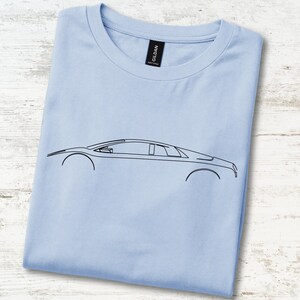 May include: A light blue t-shirt featuring a minimalist black line art illustration of a sports car in profile. The shirt has a crew neckline and a black brand label at the inner collar. The design depicts the sleek silhouette of a vehicle.