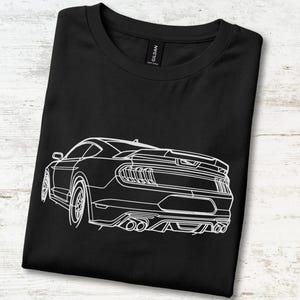 Può includere: Una t-shirt nera a girocollo con un'illustrazione a linee bianche della vista posteriore di un'auto sportiva. La grafica raffigura i fanali posteriori, lo spoiler e i doppi tubi di scarico. La maglietta ha un'etichetta nera sul collo con il testo Gildan.