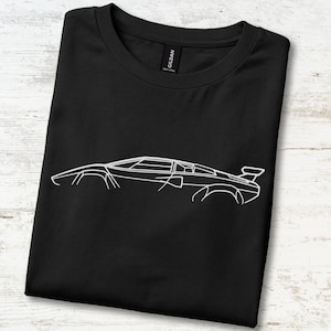 Può includere: Una t-shirt nera a maniche corte con un disegno a linee bianche di un'auto sportiva di profilo. Il design raffigura la silhouette slanciata e angolare di una classica supercar con alettone posteriore. La maglia ha un girocollo e un'etichetta Gildan.