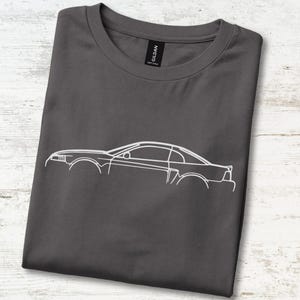May include: A dark charcoal gray crew neck t-shirt featuring a white minimalist line art illustration of a sports car in profile. The shirt has a black neck label with the brand name Gildan printed in white text visible at the collar.
