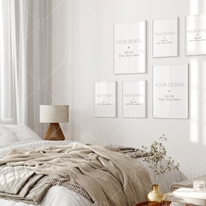 Op de afbeelding: Een witte slaapkamer met een bed, een lamp en een muur met zes witte frames. De frames zijn van verschillende grootte en hebben de tekst "YOUR DESIGN" en de grootte van het frame in inches en centimeters. De frames hangen aan een witte muur.