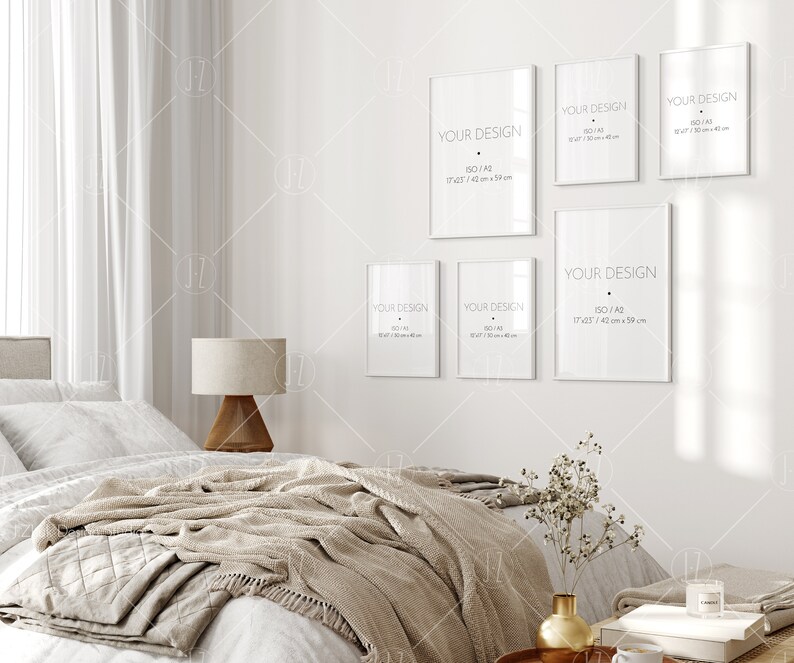 Op de afbeelding: Een witte slaapkamer met een bed, een lamp en een muur met zes witte frames. De frames zijn van verschillende grootte en hebben de tekst "YOUR DESIGN" en de grootte van het frame in inches en centimeters. De frames hangen aan een witte muur.