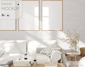 May include: A white couch with two pillows and a blanket, a coffee table with books and a diffuser, a side table with a vase of dried flowers, and two framed pictures on the wall. The room is decorated in a minimalist style with a light and airy feel.