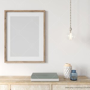 May include: A wooden frame with a white mat and a blank white interior. A light bulb hangs from the ceiling above a wooden table with a blue and white vase and a blue glass bottle. The table has a carved design.