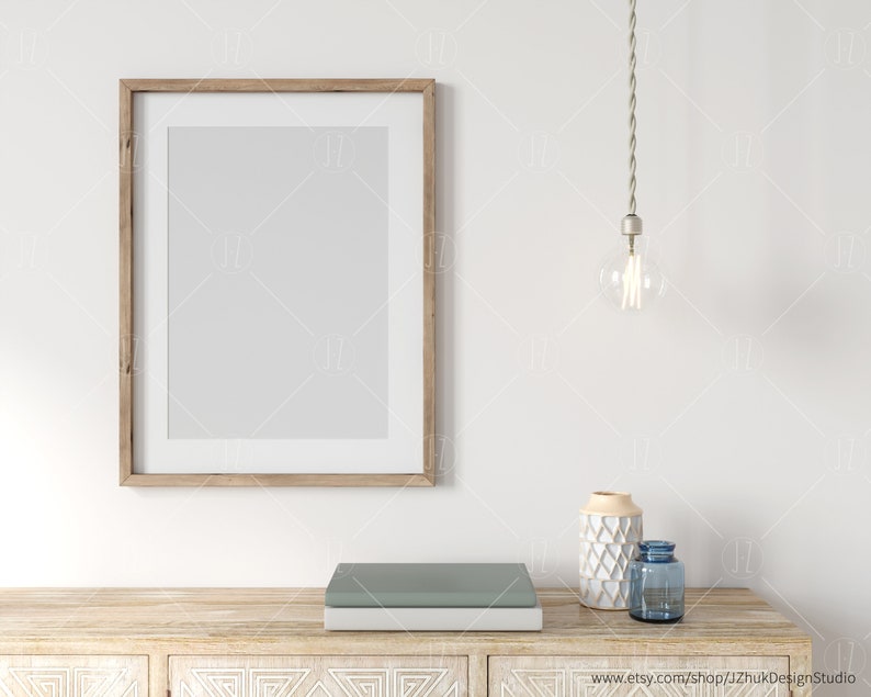 May include: A wooden frame with a white mat and a blank white interior. A light bulb hangs from the ceiling above a wooden table with a blue and white vase and a blue glass bottle. The table has a carved design.