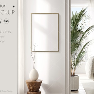 May include: A white wall with a gold frame mockup, a vase with dried branches, and a wooden stool. A large potted palm tree is visible through an open doorway.