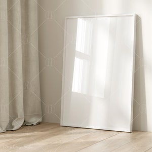 Puede incluir: Un marco de imagen blanco con un lienzo en blanco, apoyado contra una pared junto a una cortina beige.