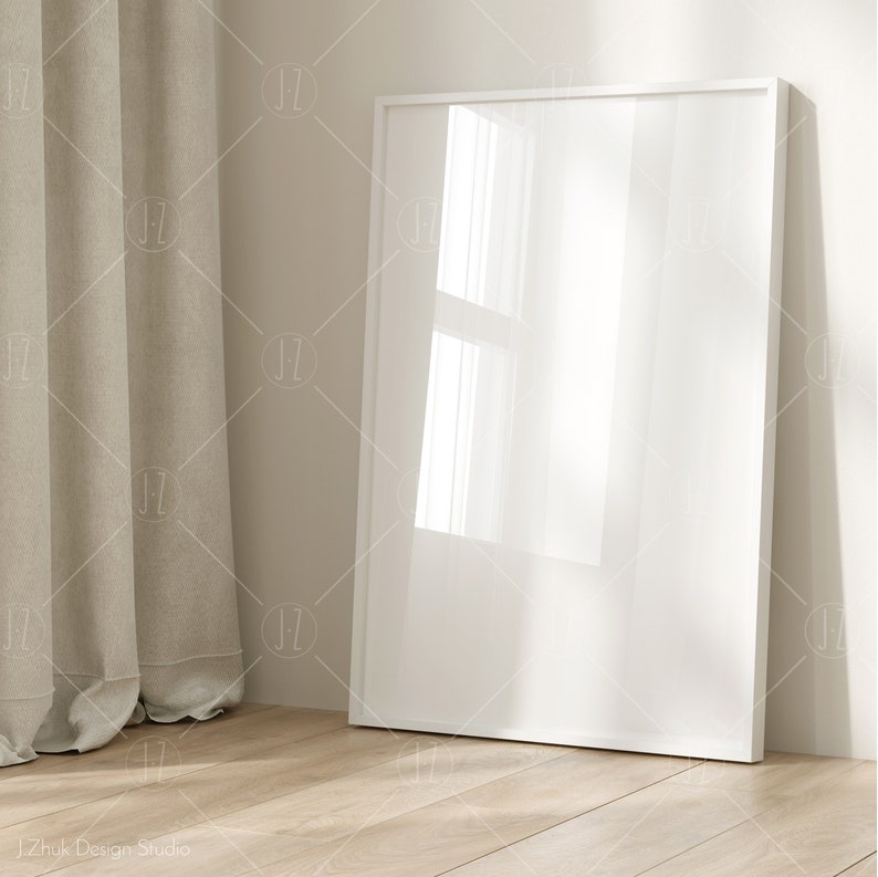 Puede incluir: Un marco de imagen blanco con un lienzo en blanco, apoyado contra una pared junto a una cortina beige.