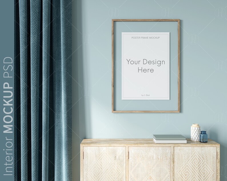May include: A light blue wall with a wooden frame poster mockup, a light blue curtain, and a wooden cabinet with a carved design. The poster mockup has the text "Your Design Here" in the center.
