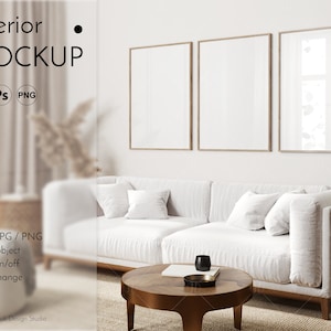 May include: A white sectional sofa with three throw pillows sits in front of a white wall with three framed pictures. A wooden coffee table with a book and a black cup sits in front of the sofa. A light brown rug is on the floor.