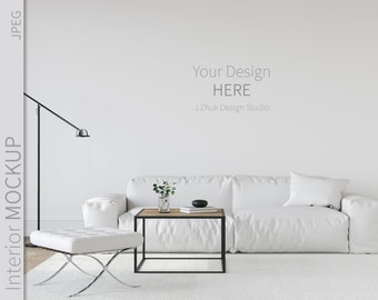 May include: A white sofa with a white throw pillow sits in a white room with a white rug. A black floor lamp is in the corner of the room. A small wooden coffee table with a vase of flowers sits in front of the sofa. The text "Your Design HERE J.Zhuk Design Studio" is on the wall.