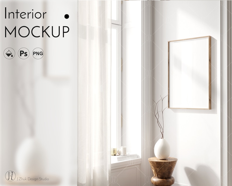 May include: A white vase with a dried branch sits on a wooden stool in front of a large, framed picture hanging on a white wall. The picture is blank and the frame is light brown. A white sheer curtain hangs in front of a window with sunlight streaming through it.