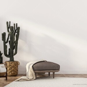 May include: A white wall with a brown ottoman with a white throw blanket in front of it. There are three potted cactus plants in the foreground.