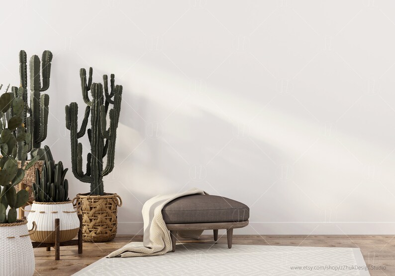 May include: A white wall with a brown ottoman with a white throw blanket in front of it. There are three potted cactus plants in the foreground.