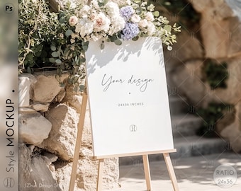 May include: A white sign on a wooden easel, adorned with floral arrangements. The sign reads "Your design" and "24x36 inches". The sign is part of a wedding or event mockup, with a stone wall and greenery in the background.