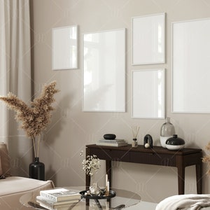 May include: A living room interior with a beige couch, a glass coffee table, and a console table with a vase, candles, and books. There are five white picture frames on the wall, two of which are vertical and three of which are horizontal.