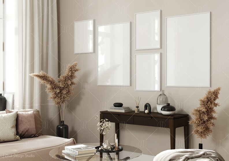 May include: A living room interior with a beige couch, a glass coffee table, and a console table with a vase, candles, and books. There are five white picture frames on the wall, two of which are vertical and three of which are horizontal.