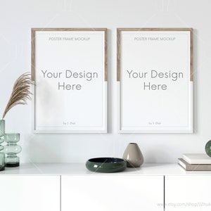 Puede incluir: Dos carteles enmarcados en blanco con el texto "Your Design Here" en una pared blanca sobre una cómoda blanca con un cuenco verde, un jarrón con flores secas y un jarrón beige.