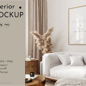 Puede incluir: Un sofá blanco con dos almohadas se encuentra en una sala de estar con una cortina beige y una mesa auxiliar de madera. Un póster enmarcado con el texto "YOUR DESIGN ISO/AO 33x47/84 cm x 119 cm" cuelga de la pared.