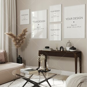 May include: A living room interior with a beige sofa, a glass coffee table, a console table with a vase and candles, and four white framed prints with the text "Your Design" and different size ratios. The prints are hung on a beige wall.